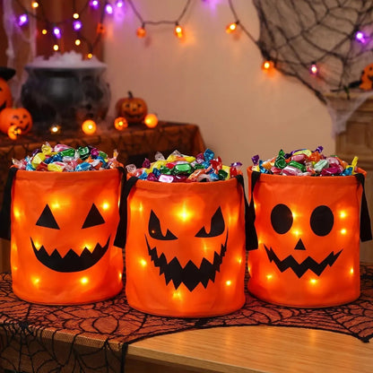 Three orange LED candy buckets full of wrapped candy on a spiderweb table runner