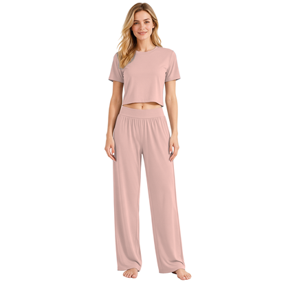 Pink colourway — AI-generated studio image of an adult model wearing the two-piece pyjama set (short cropped crew-neck tee with exposed midriff, wide elastic high-waist wide-leg trousers)